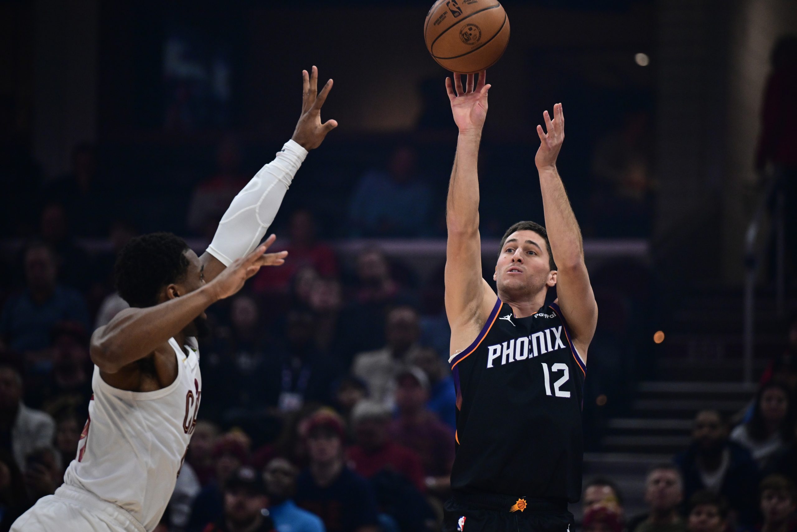 Dec 31, 2025; Cleveland, Ohio, USA; Phoenix Suns guard Collin Gillespie (12) shoots a three point shot over rCleveland Cavaliers guard Donovan Mitchell (45) during the first half at Rocket Arena. Mandatory Credit: David Dermer-Imagn Images